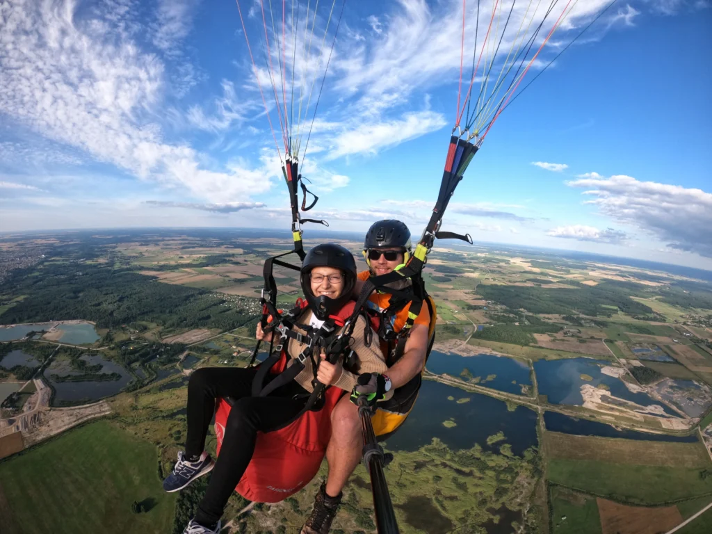 Parasparniu skrendantys žmonės aukštai virš vakarų Lietuvos